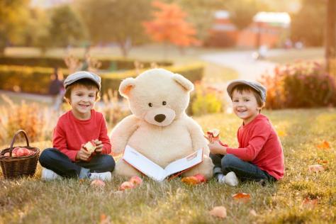 Two boys eating apples with a large teddy bear sitting between them
