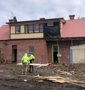 Construction workers cutting wood in front of a brick cottage