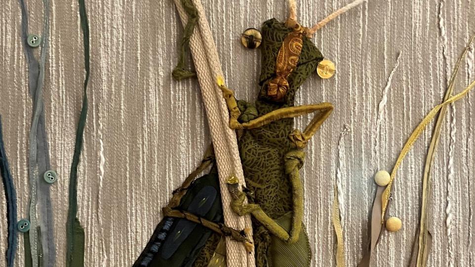 An embroidered cricket on a silver fabric background