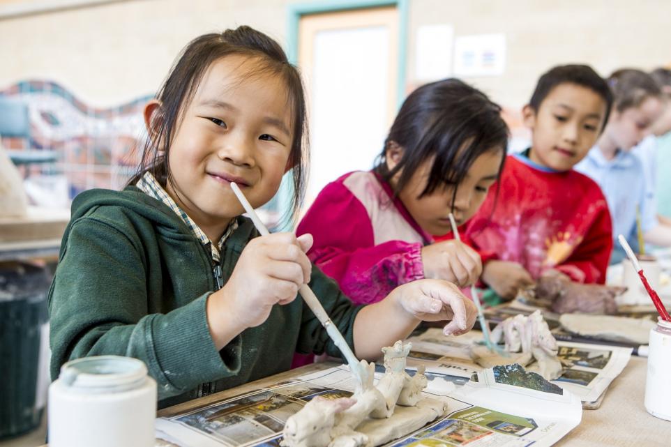 three children in pottery studio painting clay artworks