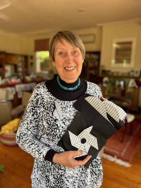 Smiling woman holding up quilted fabric.