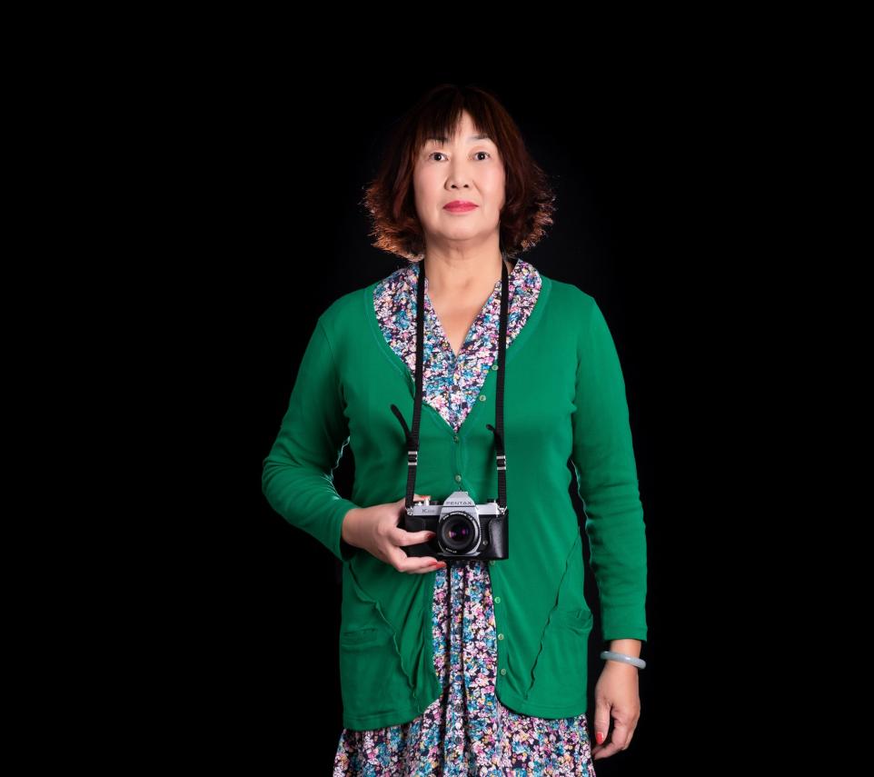 Portrait of a Chinese lady wearing a green cardigan and holding a camera