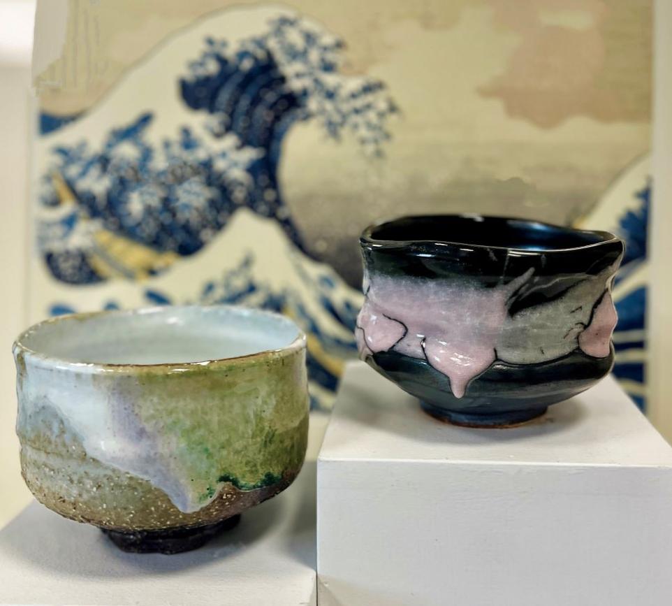 Two hand made pottery tea bowls sitting in front of a Japanese print