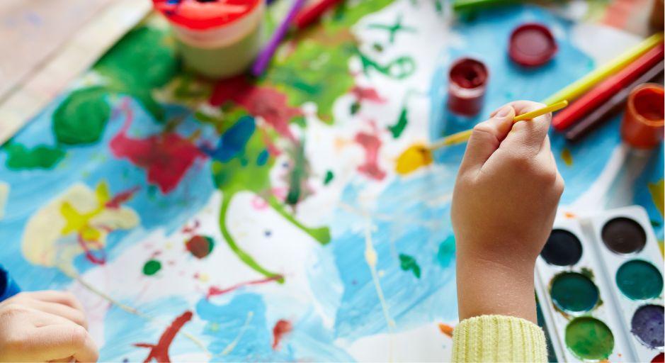 child hand holding a brush painting with watercolours