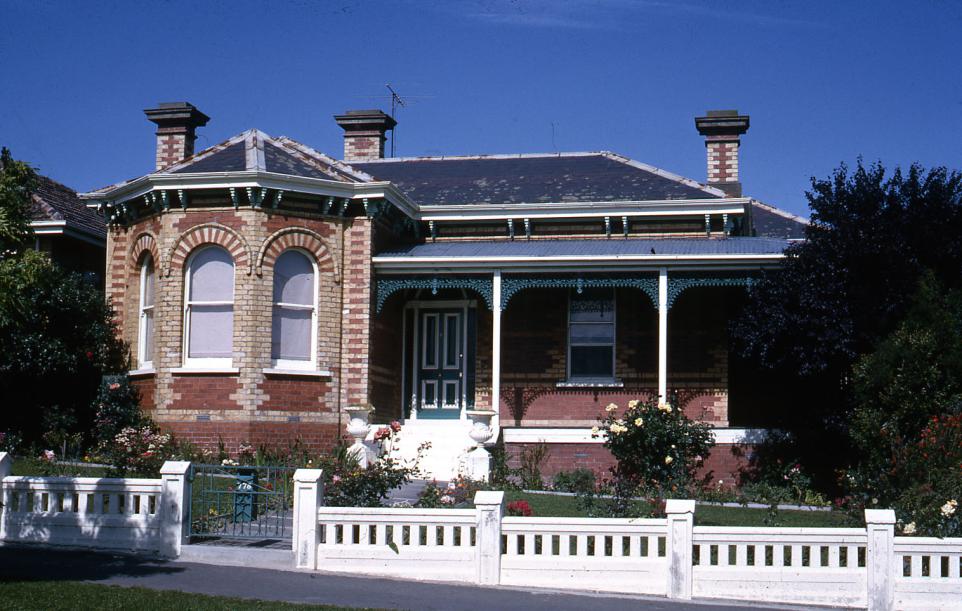 Brick bungalow with verandah and white fence.