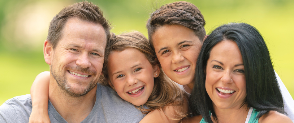 Photograph of a family smiling at the camera, mum, dad and two children