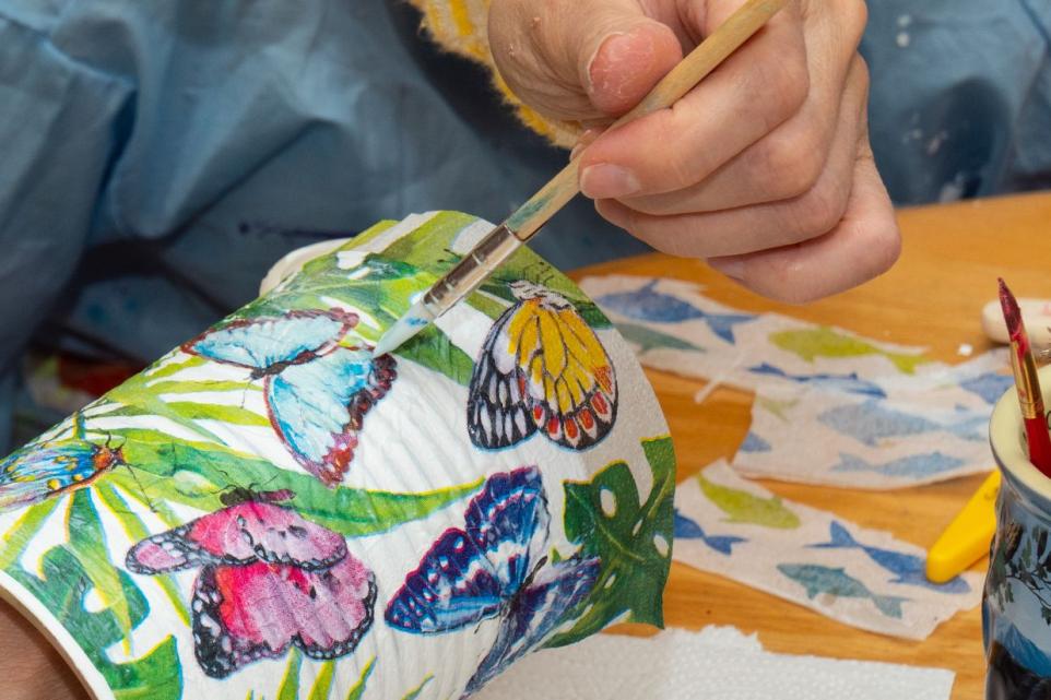 person creating decorative pencil holder with butterfly fabric. 