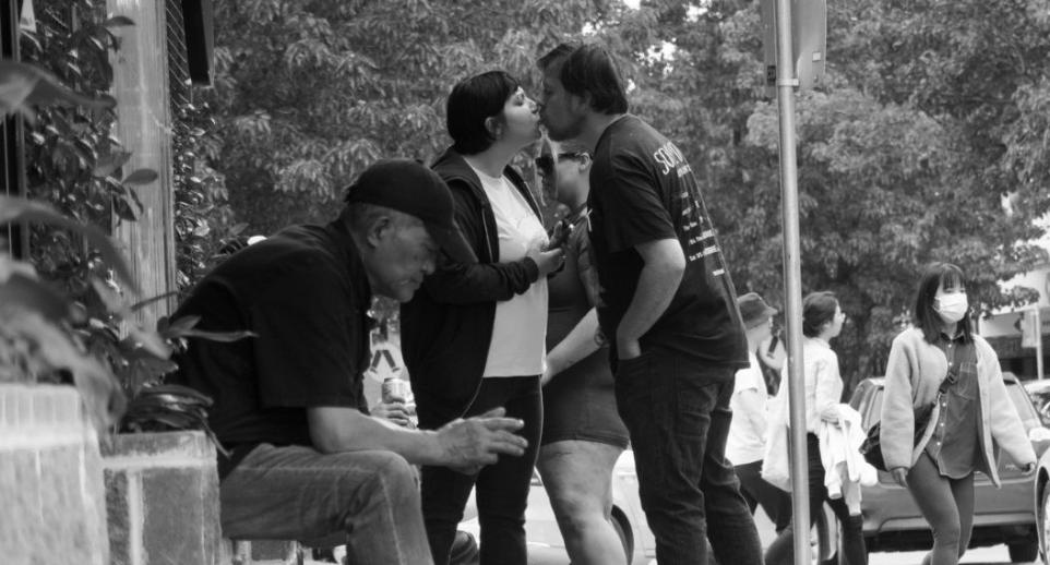 Black and white photo of a street scene, two people kissing.