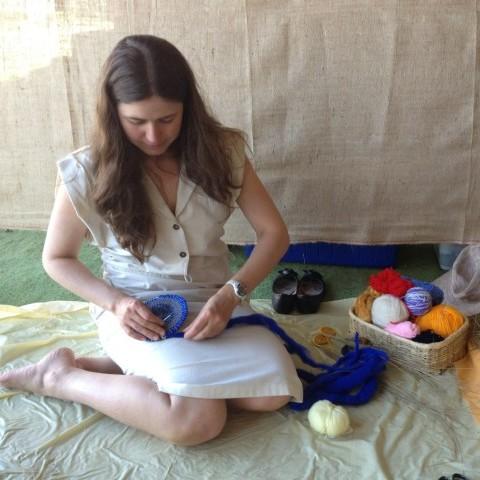 A women with long brown hair sitting on the floor weaving a basket with blue yarn