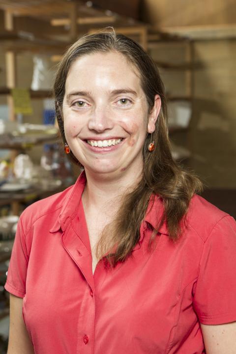 A lady with brown hair in a red shirt smiling at the camera