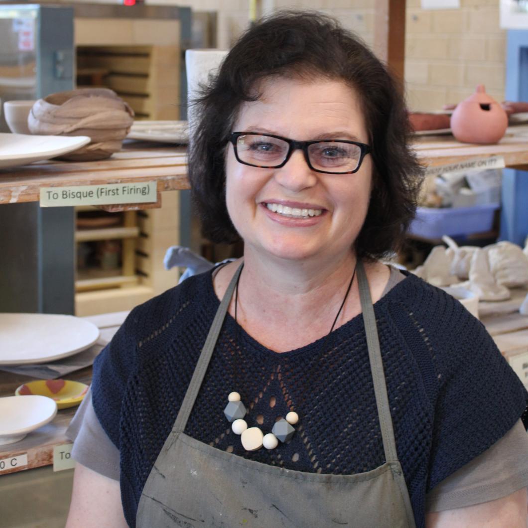A lady with short brown hair in a black t-shirt and apron smiling at the camera