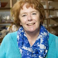 A lady with short red hair with a blue shirt and scarf smiling at the camera