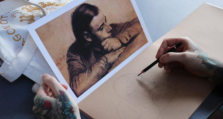 Artist sketching a portrait based on an image in front of them