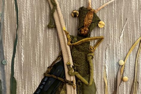 An embroidered cricket on a silver fabric background