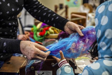 An older woman's hands holding coloured wool with a child's hand touching the wool.