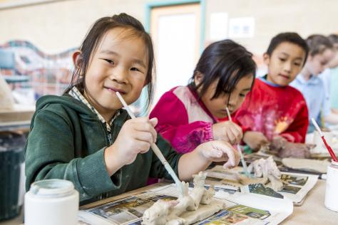 three children in pottery studio painting clay artworks