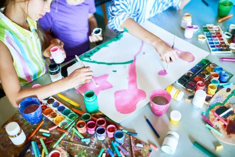 a table of art materials and kids doing colourful painting