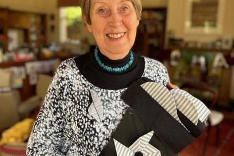 Smiling woman holding up quilted fabric.