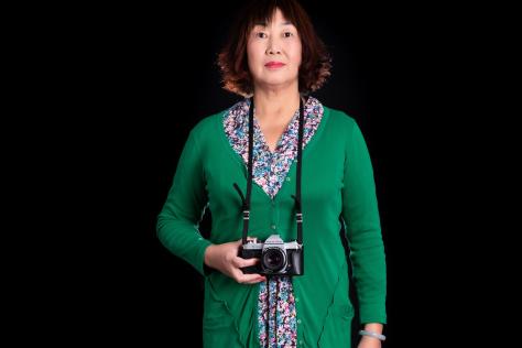 Portrait of a Chinese lady wearing a green cardigan and holding a camera