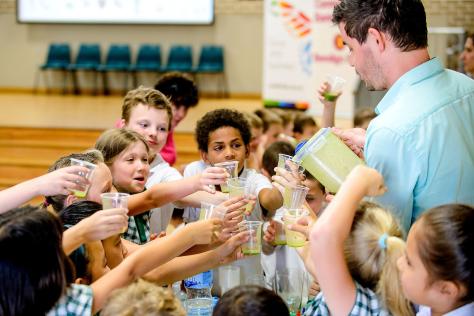 children holding glasses up to drink a green smoothie. 