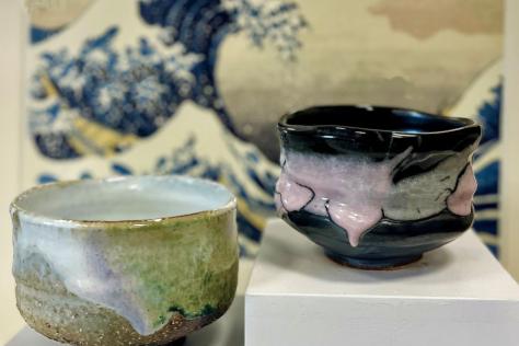 Two hand made pottery tea bowls sitting in front of a Japanese print