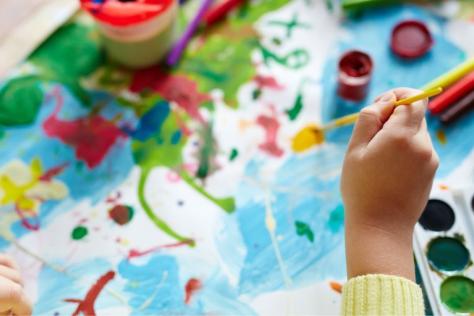 child hand holding a brush painting with watercolours