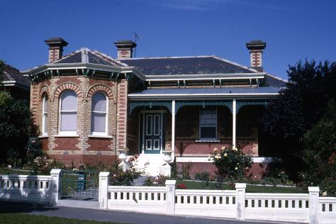 Brick bungalow with verandah and white fence.