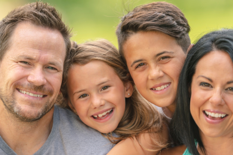 Photograph of a family smiling at the camera, mum, dad and two children