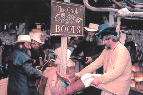 Historic photo of three men trying on country boots and hats for sale