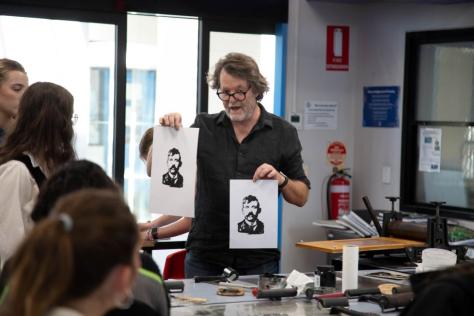 An artist holding up two prints during a workshop.