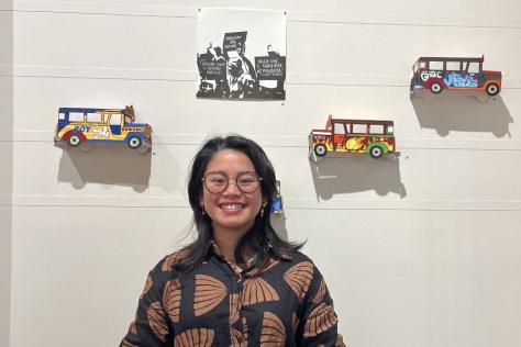 Photograph of an artist engaging the camera in front of a wall with their art