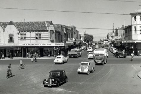 Black and white photograph showing cars driving past buildings on Whitehorse Road.