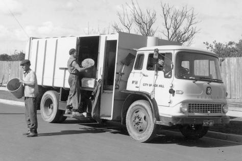 Black and white photograph showing a white truck and two garbage men.