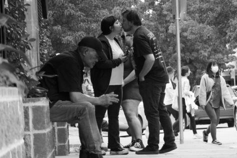 Black and white photo of a street scene, two people kissing.