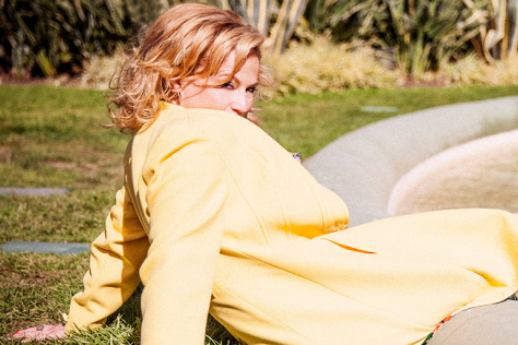 A lady sits on the ground leaning backwards on a very sunny day.