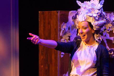 A performer smiles and points in a large paper headdress