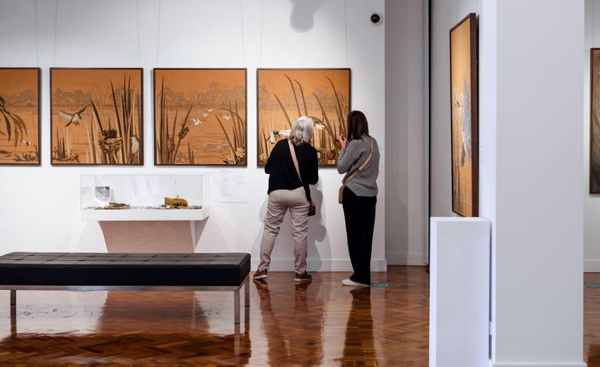 Two people in a gallery looking at a large textile art piece.