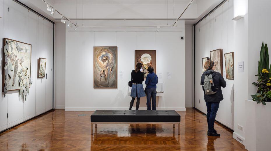 Three people in a gallery viewing textile art